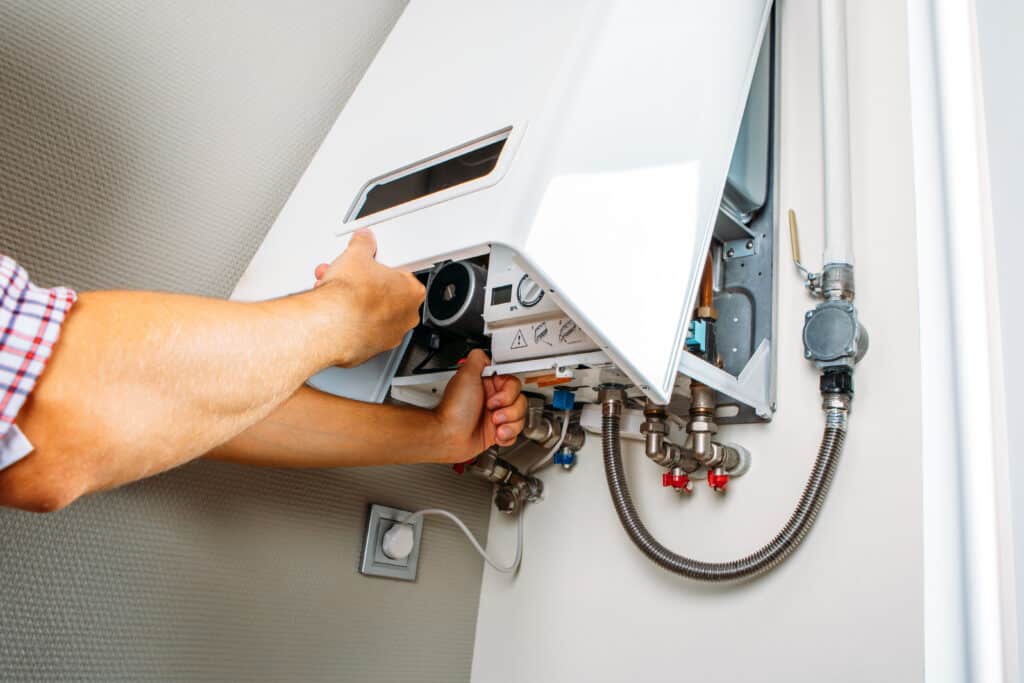 Chauffagiste effectuant la maintenance d’une chaudière murale dans un logement, capot ouvert, outils en main, lors d’une intervention de dépannage ou d’entretien.